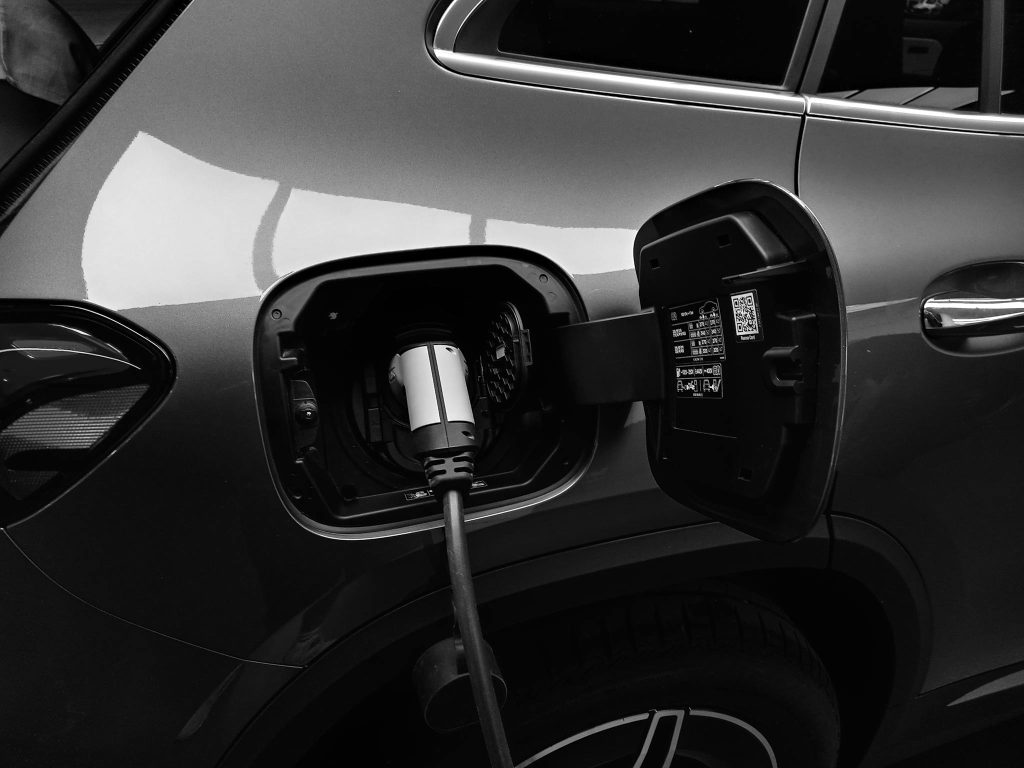 Close-up black and white image of an electric vehicle charging at a station.